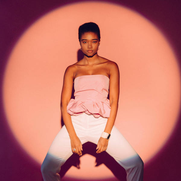 Studio shot of a Black male model wearing a white tank top against a gray gradient background, striking a confident pose under soft lighting.