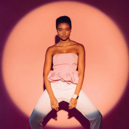 Studio shot of a Black male model wearing a white tank top against a gray gradient background, striking a confident pose under soft lighting.