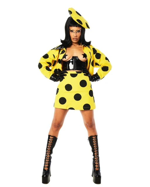 Full-length shot of a woman in a yellow polka-dot outfit with a corset, gloves, and platform boots, standing against a white backdrop.