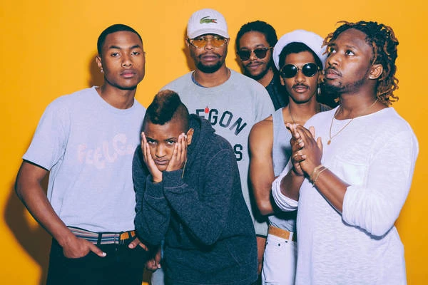 Group portrait of five young Black men in casual attire against a vibrant yellow backdrop, showcasing diverse styles and expressions.