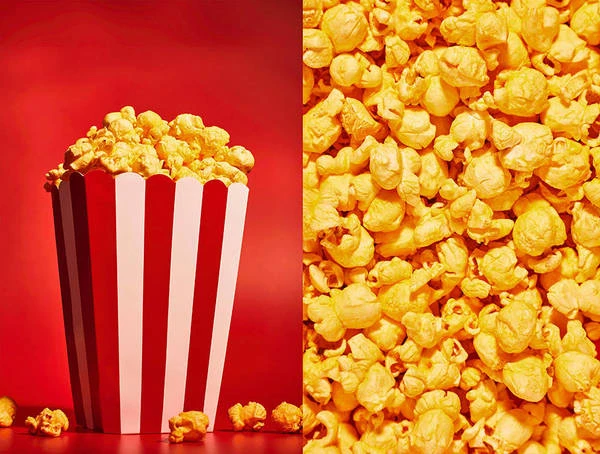 Popcorn overflowing from a red and white striped container sits on a red surface, with a close-up view of scattered popcorn kernels beside it.