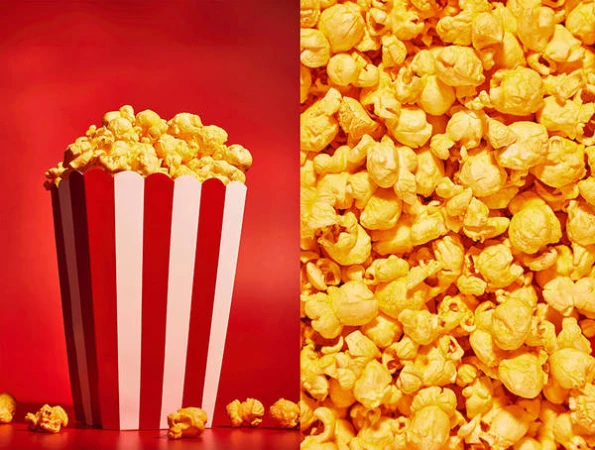 Popcorn overflowing from a red and white striped container sits on a red surface, with a close-up view of scattered popcorn kernels beside it.