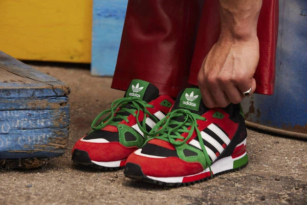 Close-up of Adidas sneakers in red, green, and white being tied by a person wearing red leather pants.