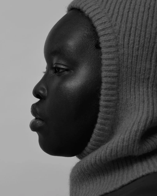 Monochromatic portrait of an African-descent adult female in profile wearing a knit hood, with soft lighting and a plain background.