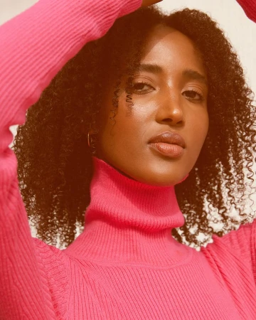 Black woman with curly hair wearing a bright pink turtleneck sweater posing for photographer Katy Pritchett