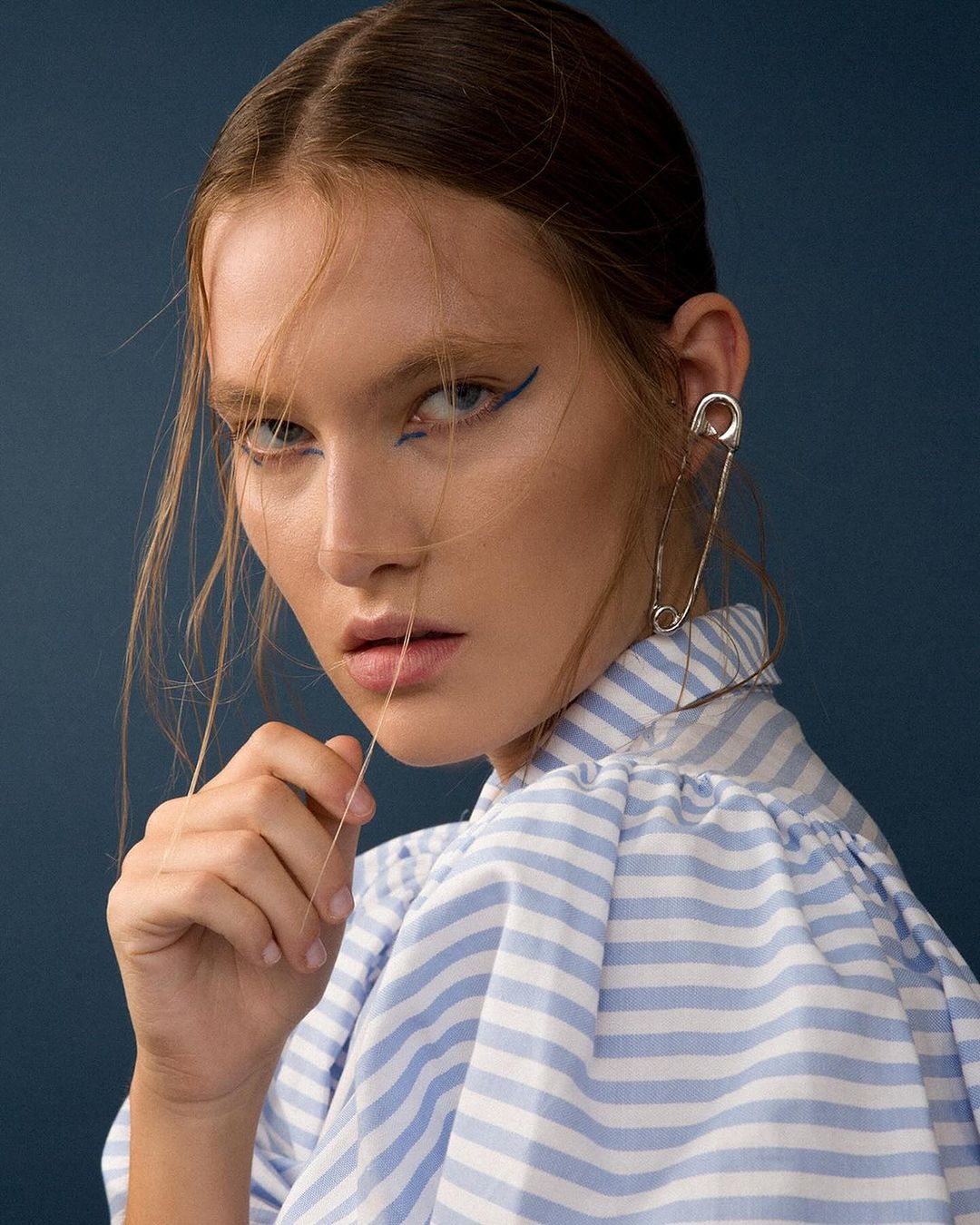 Portrait of a woman wearing a blue and white striped shirt and a large silver safety pin earring by Katy Pritchett.