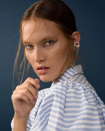 Portrait of a woman wearing a blue and white striped shirt and a large silver safety pin earring by Katy Pritchett.