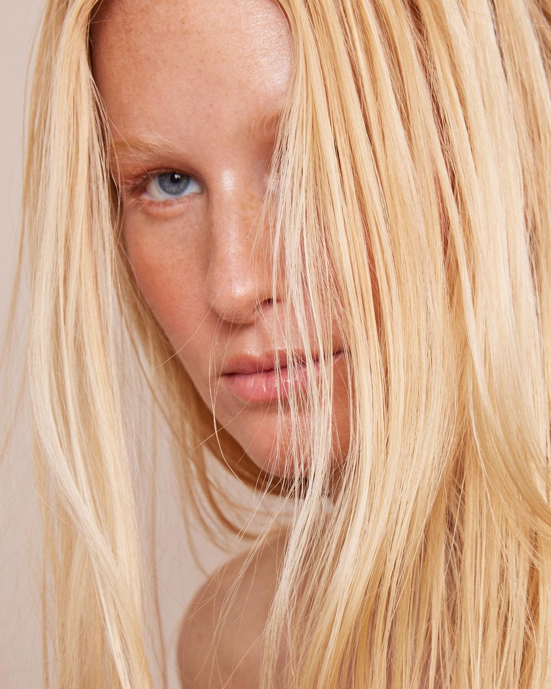 Close-up portrait of a fair-skinned adult female with striking blue eyes and flowing blonde hair partially covering her face.