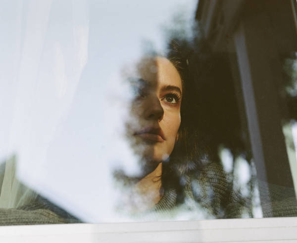 Portrait of a woman wearing a green sweater viewed through a window with reflections