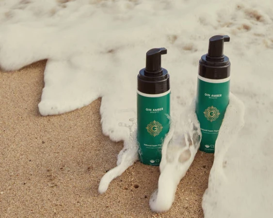 Two green foam pump bottles resting on wet sand as ocean waves wash around them.