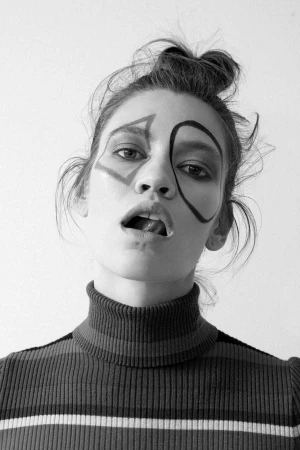 Black and white portrait of a woman wearing a striped turtleneck with geometric face makeup and hair tied up in a topknot