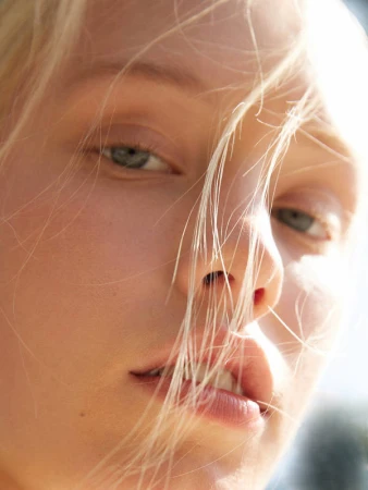 Close-up portrait of a fair-skinned woman with blonde hair falling across her face in bright sunlight