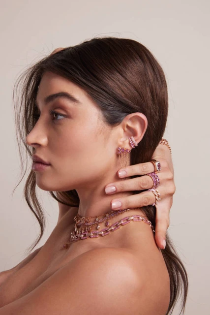 Profile shot of a young brunette female model wearing pink gemstone earrings, rings and necklace. Beauty and jewelry product shot.
