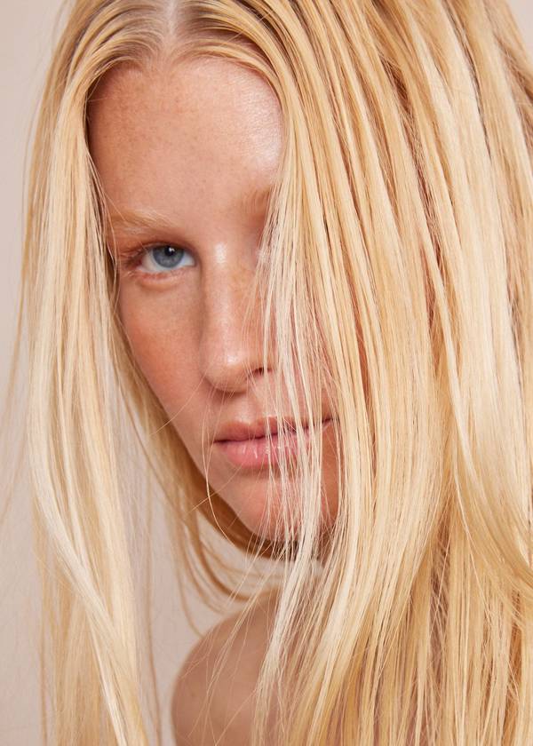 Close up portrait of a blonde woman with blue eyes and strands of hair across her face photographed by Katy Pritchett.