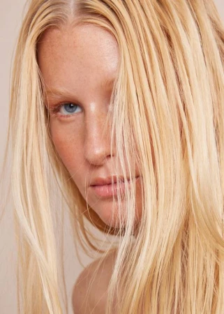 Close up portrait of a blonde woman with blue eyes and strands of hair across her face photographed by Katy Pritchett.