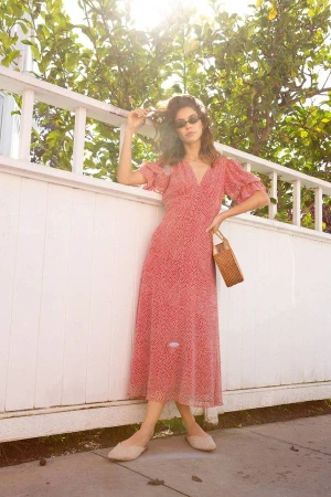 Woman in red patterned midi dress and sunglasses leaning against a white wooden fence under lemon trees