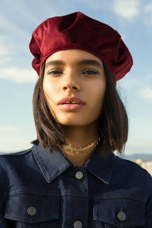 Model wearing a deep red velvet beret and a dark blue denim jacket against a clear sky background