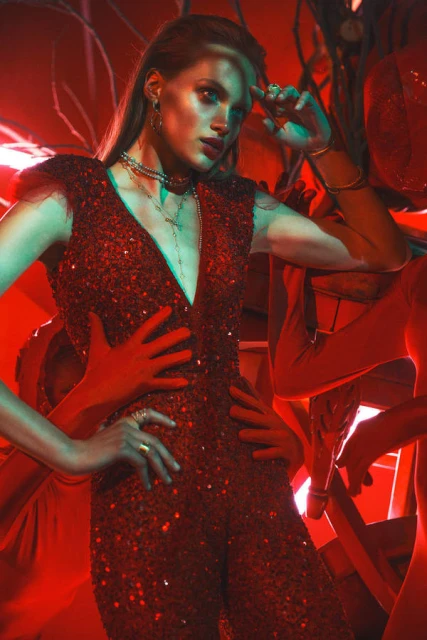 Woman in red sequin jumpsuit surrounded by hands and red lighting, jewelry, and evening wear fashion, studio shot.