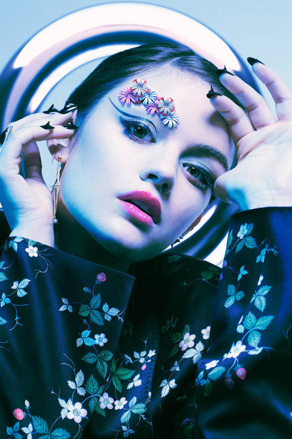 Close-up of a young woman with creative makeup including floral accents around her eye, wearing a floral patterned robe and earrings.