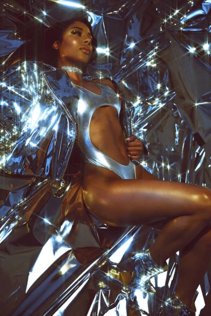 Elegant woman poses in a reflective silver swimsuit and jacket, lying against shiny, silver metallic backdrop, fashion and beauty photoshoot.