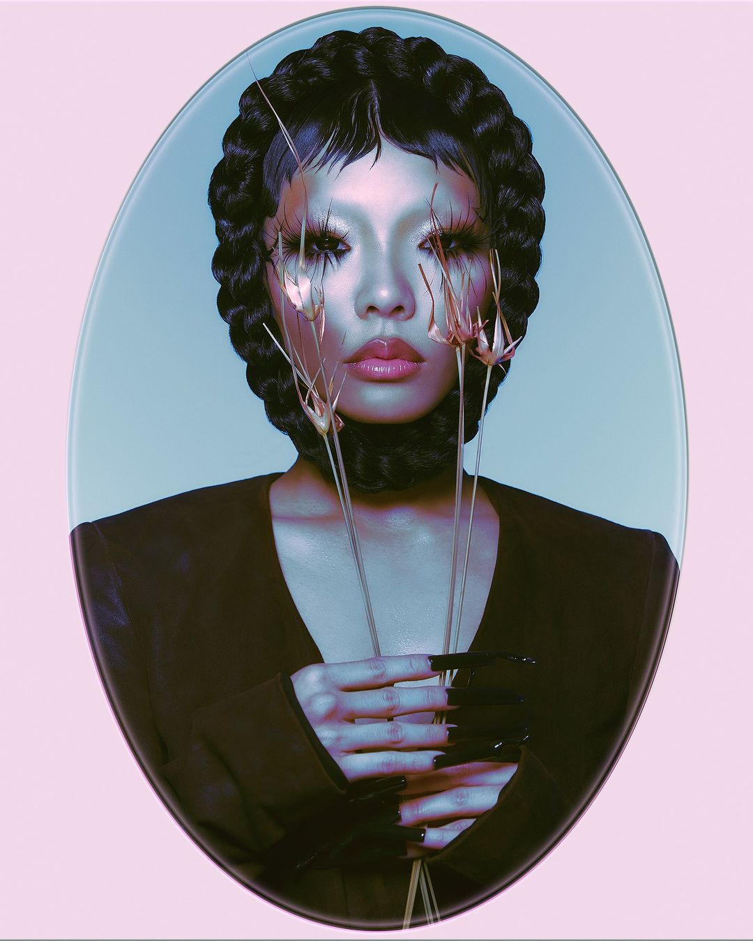 Striking beauty shot of a woman with dramatic makeup and black braided hair, holding dried floral elements against an oval backdrop.