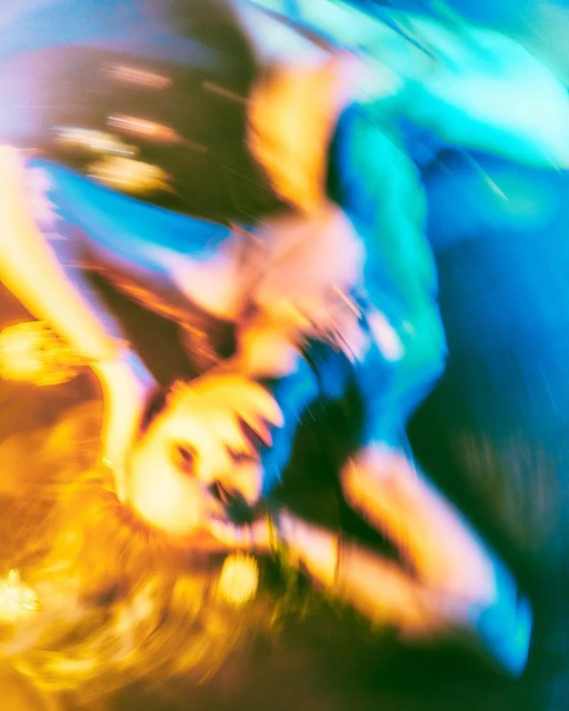 Blurred motion shot of an adult female in a blue outfit, dynamic movement effect, with a blend of orange, yellow, and blue lighting.