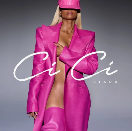 Singer Ciara poses wearing a pink leather outfit consisting of a hat, jacket, and thigh-high boots against a gray background.