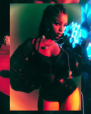 Portrait of a woman in a black bodysuit and sparkling shrug with cornrow braids, posed against a two-toned green and orange background.