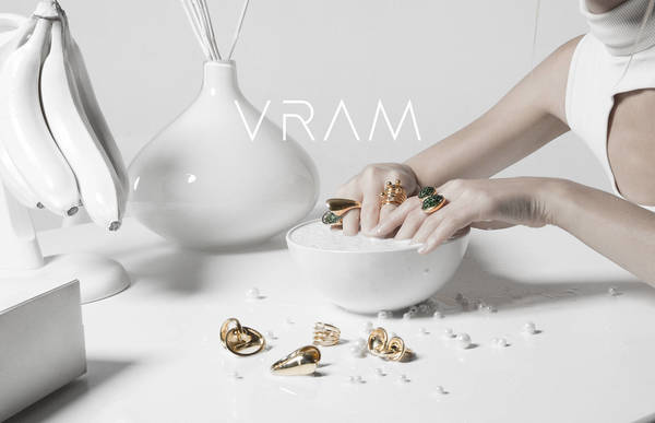 Close-up of rings on fingers and tabletop with vase, bananas, and white pearls creating a beauty product-shot aesthetic.