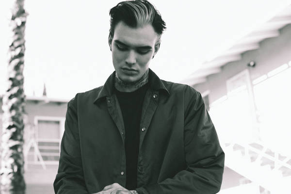 Monochrome portrait of a young adult man with dark hair, wearing a collared jacket. He looks down with a serious expression.