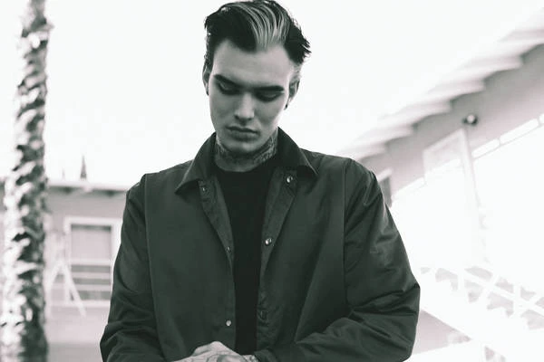 Monochrome portrait of a young adult man with dark hair, wearing a collared jacket. He looks down with a serious expression.