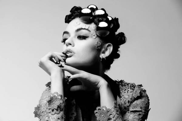 Black-and-white portrait of a woman with reflective curlers in her hair, showcasing dramatic makeup and lace details on her clothing.