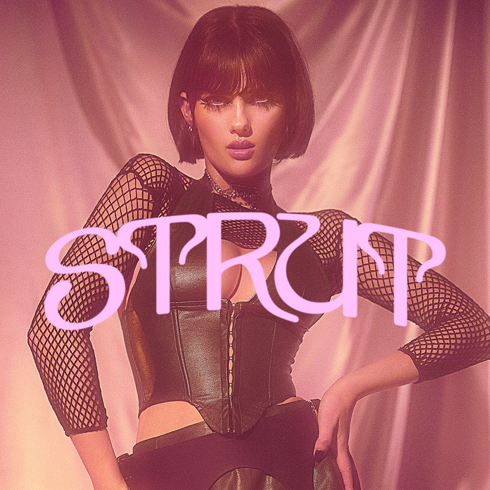 Portrait of a woman with dark hair in a black corset and fishnet sleeves with 'STRUT' text overlayed on a pink background.