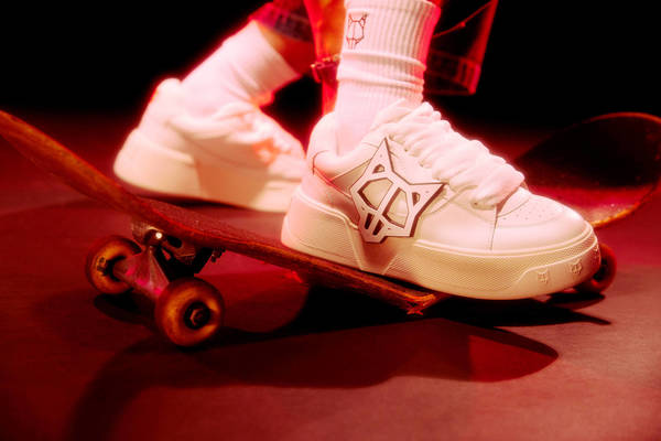 Low angle shot of white chunky sneakers and white socks standing on a skateboard under red lighting by Brian Ziff.