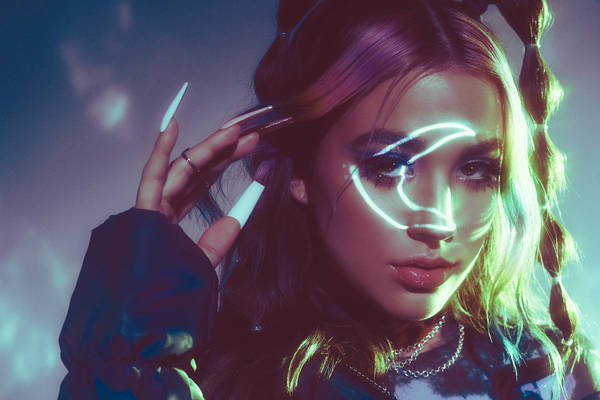 Portrait of a woman with long hair, light-up makeup, and long white nails in a studio setting, showcasing fashion and beauty elements.