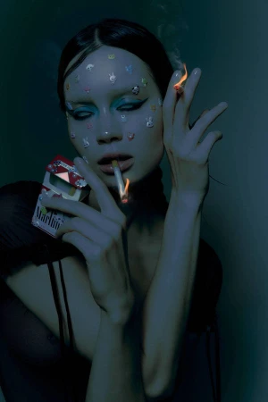 Portrait of a woman with face stickers, blue eyeshadow, holding a cigarette and a pack, photographed by Brian Ziff