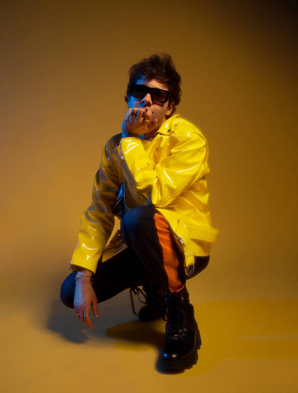 Brian Ziff portrait: A male musician stands against a textured background in a dimly lit photo studio. He wears a hat and holds a guitar.