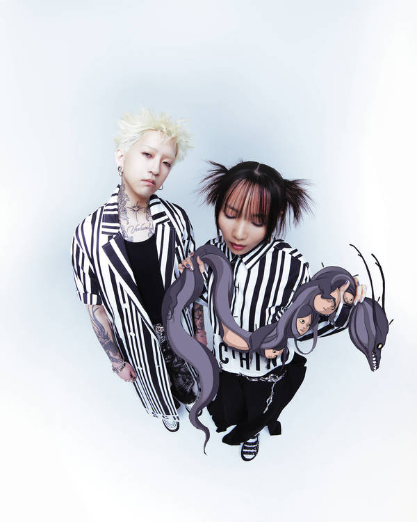 Low-angle shot of a young adult non-binary couple posing in matching striped shirts and dark pants against a white background with octopus prop.