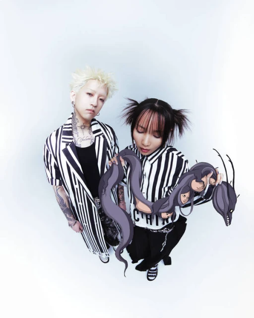 Low-angle shot of a young adult non-binary couple posing in matching striped shirts and dark pants against a white background with octopus prop.
