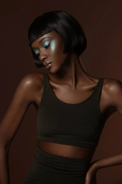Close-up studio shot of an adult woman with short dark hair and blue eyeshadow, wearing a dark-colored top, looking downward.