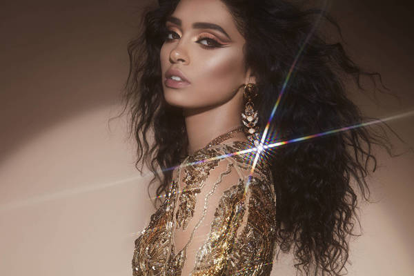 Portrait of a woman with dark curly hair wearing a shimmering gold embroidered dress and statement earrings by Brian Ziff.