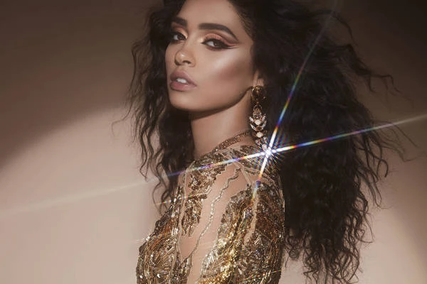 Portrait of a woman with dark curly hair wearing a shimmering gold embroidered dress and statement earrings by Brian Ziff.