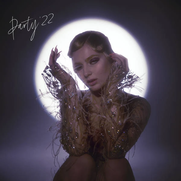 Close-up portrait of a young woman with an elegant hairstyle and glittering feathered attire, posing in front of a spotlight.