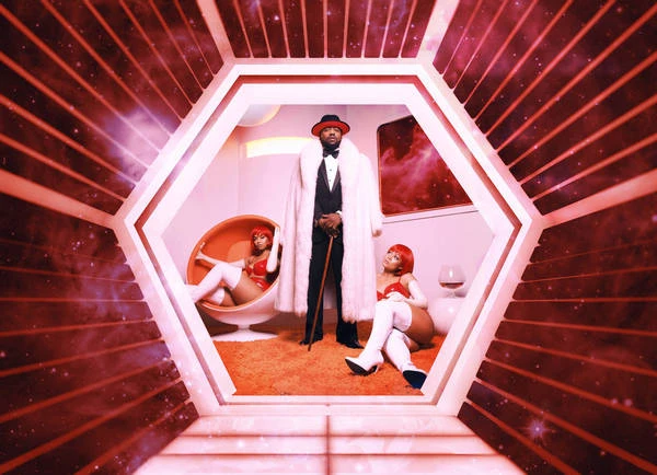 Man in a fur coat and hat stands in a retro-futuristic room with two women in red outfits. The room has an orange floor.