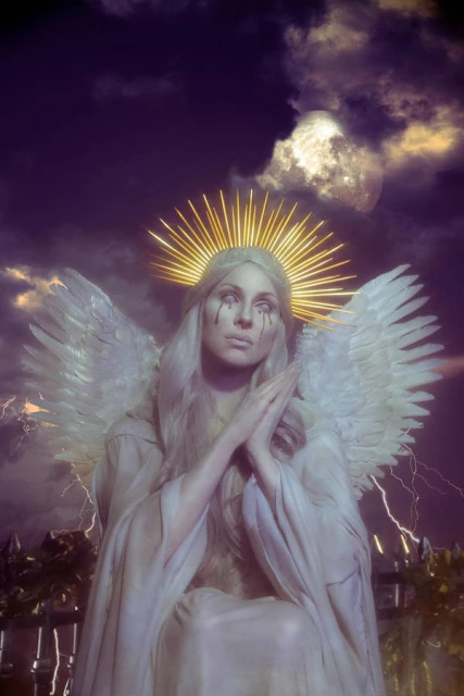 Woman in angel costume with tears sitting against a dramatic sky with lightning and a full moon. Fantasy photography in an outdoor setting.