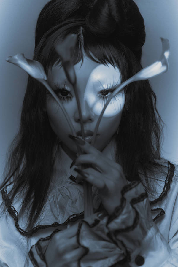Monochromatic portrait of an Asian woman with white face paint, long black hair and holding white calla lilies up to her face.