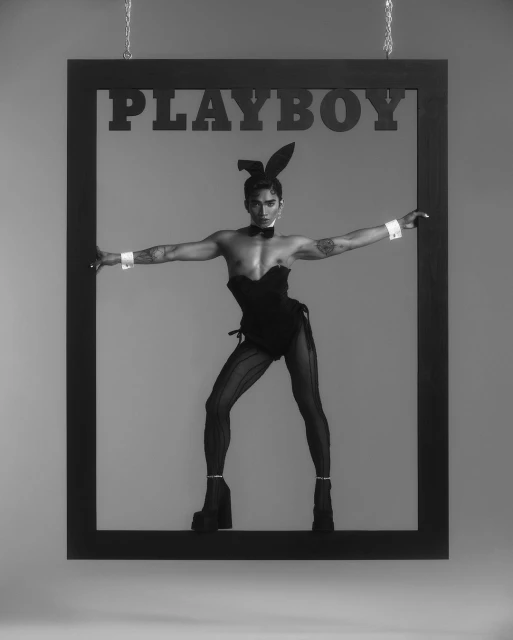 Man wearing bunny ears and a bodysuit strikes a pose within a black picture frame, resembling a vintage Playboy magazine cover.