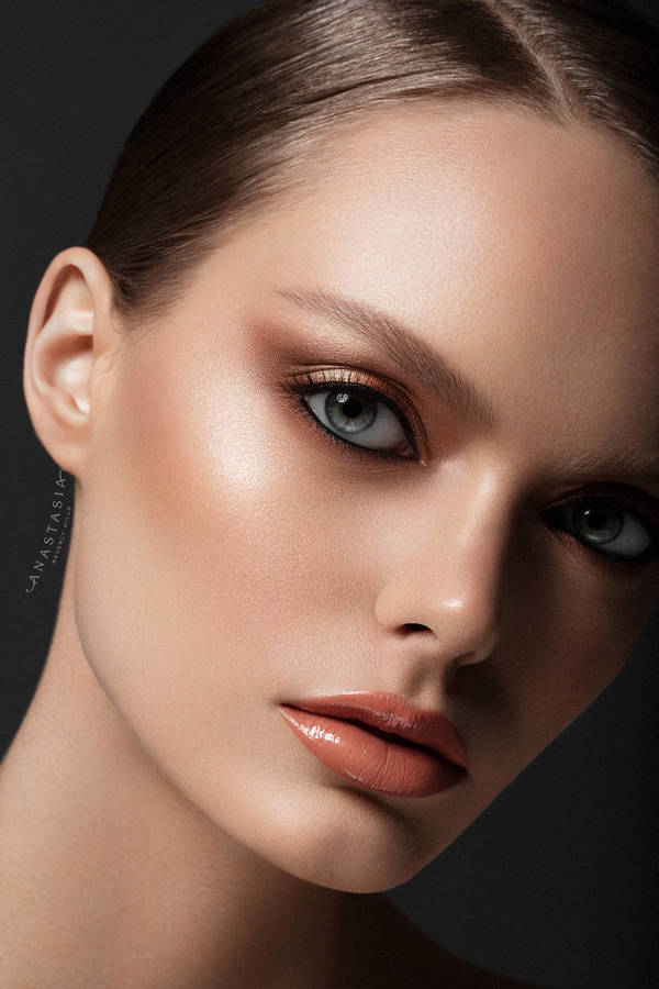 Close-up portrait of a fair-skinned woman with light brown hair, soft brown eyeshadow, glossy nude lipstick, and a neutral facial expression.
