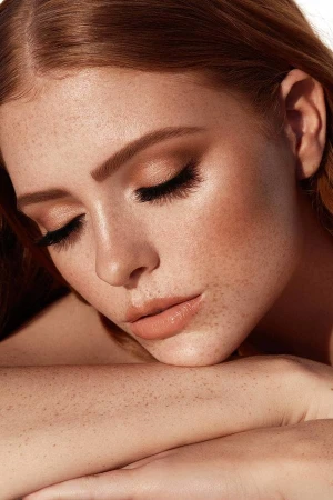 Close up portrait of a freckled woman with closed eyes resting her head on her arms by Brian Ziff