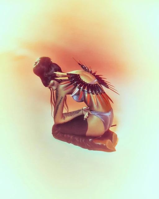 Woman kneeling with fantasy-inspired wings. The portrait showcases hair, body art, and fashion details in a surreal and artistic composition.